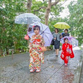 雨の中、傘をさして移動する七五三記念日の家族