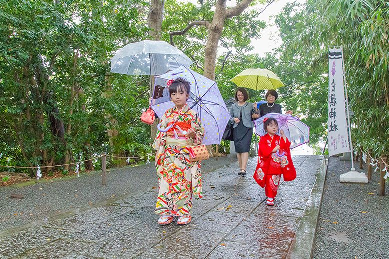 雨の中、傘をさして移動する七五三記念日の家族